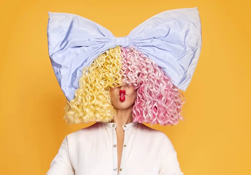 Sia wearing signature oversized yellow and pink colored wig with baby blue bow