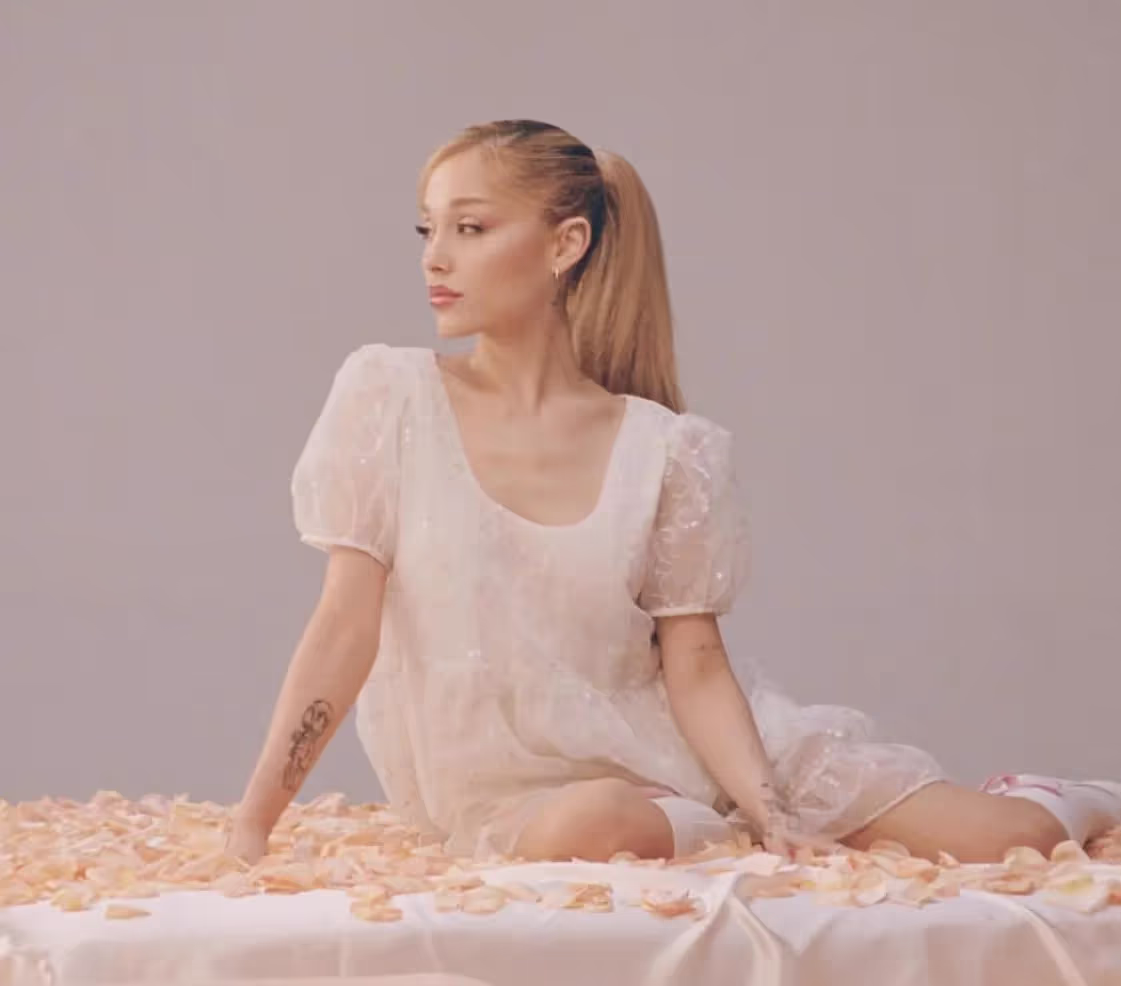 Ariana Grande sitting on bed surrounded by rose petals, eternal sunshine earns platinum RIAA certification