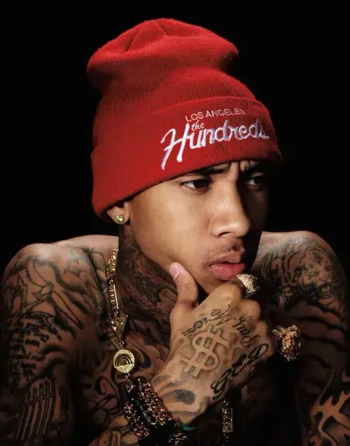 Tyga wearing a red hat, showcasing his tattoos, celebrating 'Taste' achieving RIAA Diamond status.