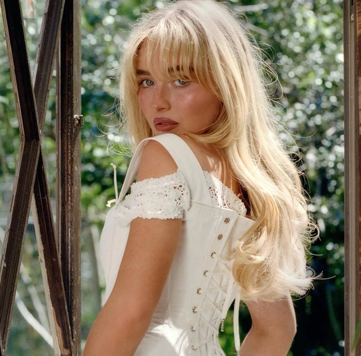 Sabrina Carpenter wearing a white lacy corset, looking over her shoulder, celebrating 'Short n' Sweet' RIAA Platinum certification.