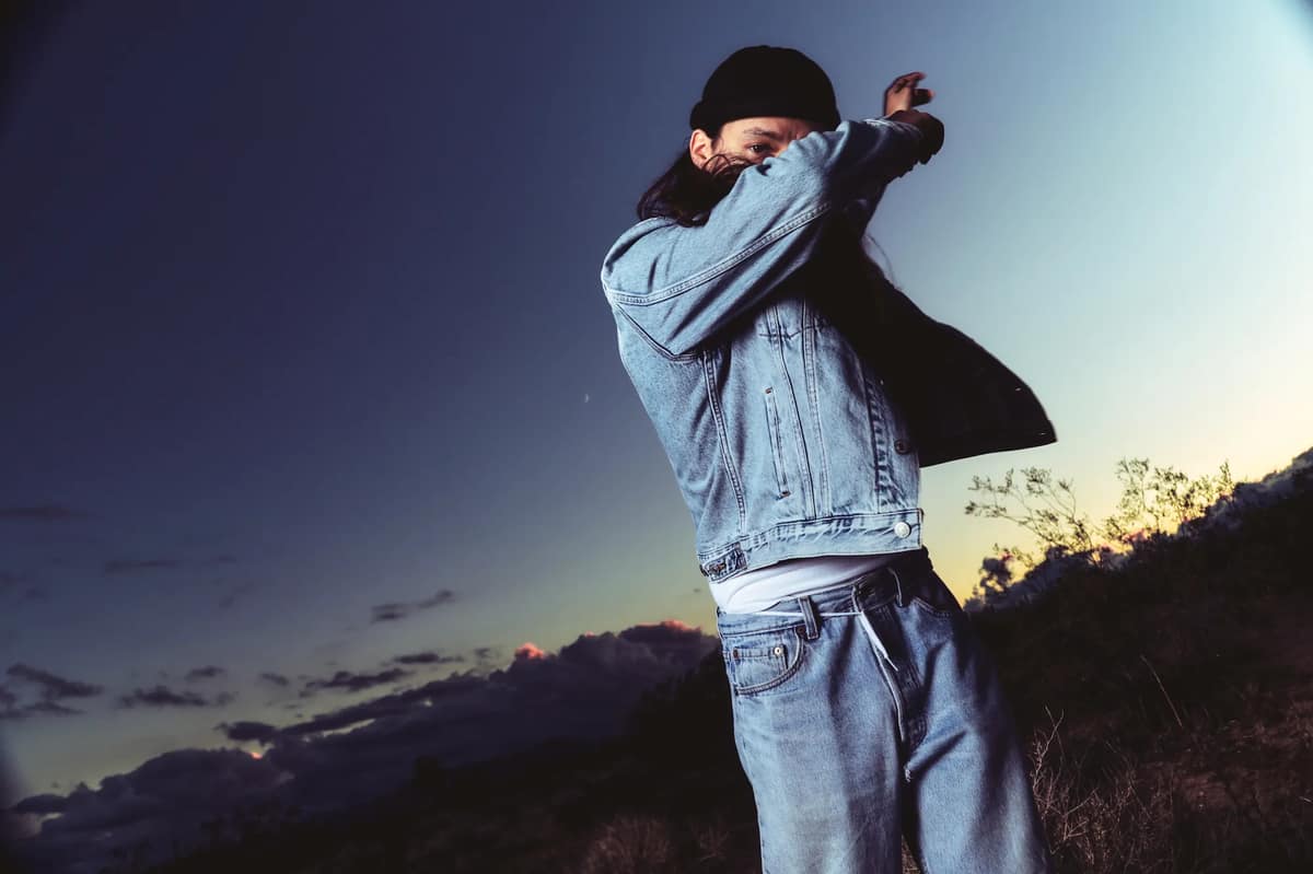 Sunsetto, wearing black hat, jeans, jeans jacket. Photo Credit: @blacksocks.studio