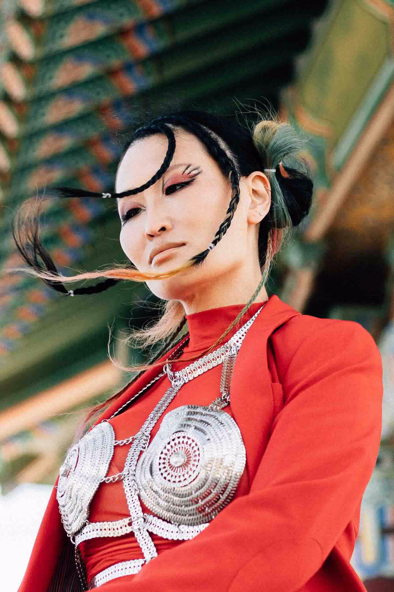 A portrait of Nolo Grace wearing a red suit and a metal bralette