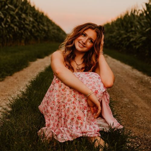 Stella Mabry seated on a country lane in a pink floral dress at sunset.